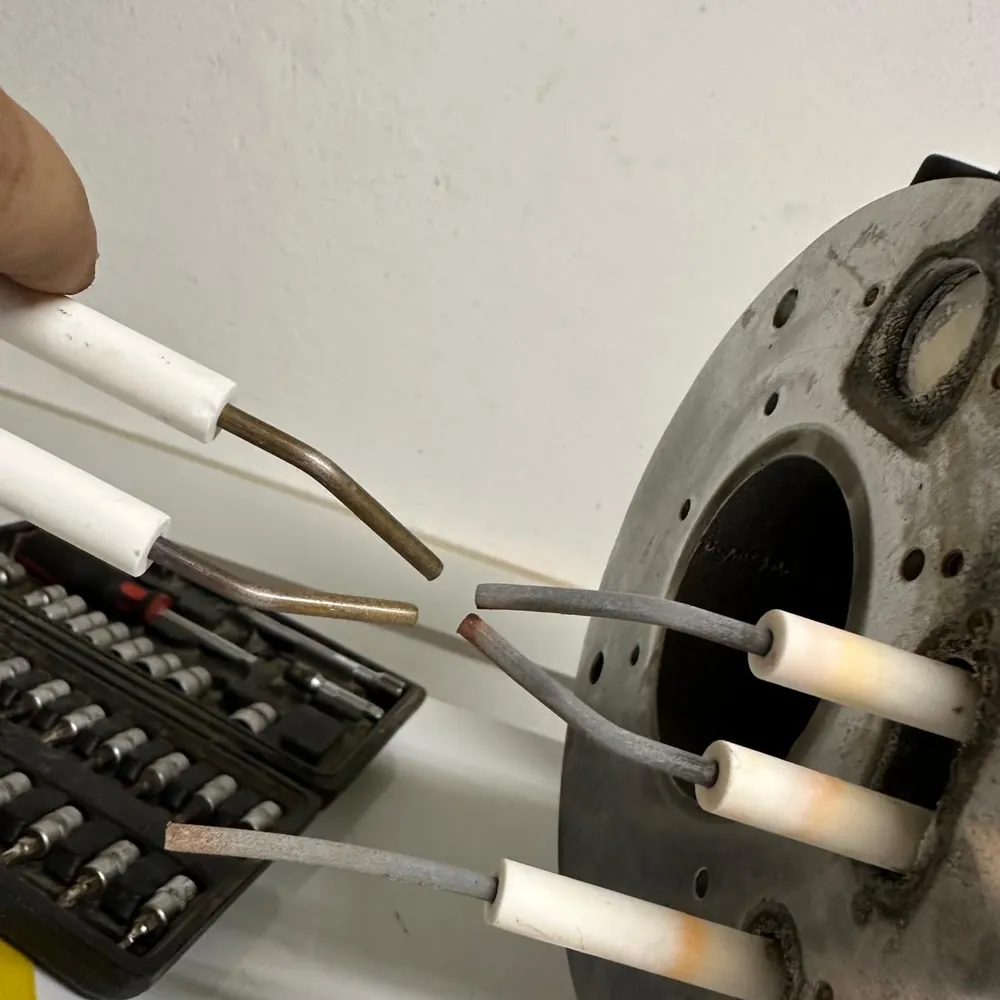Verschlissene Zündelektroden am Brennerflansch, daneben neue Elektroden